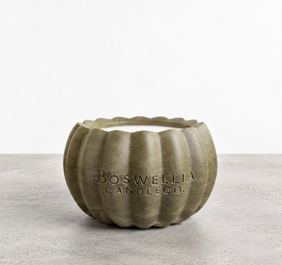 Front view of a pumpkin-shaped concrete candle in smoky olive green, with white wax and Boswellia Candle Co. engraved on the vessel.