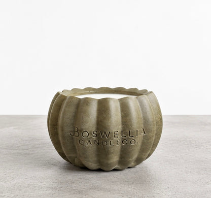 Front view of a pumpkin-shaped concrete candle in smoky olive green, with white wax and Boswellia Candle Co. engraved on the vessel.