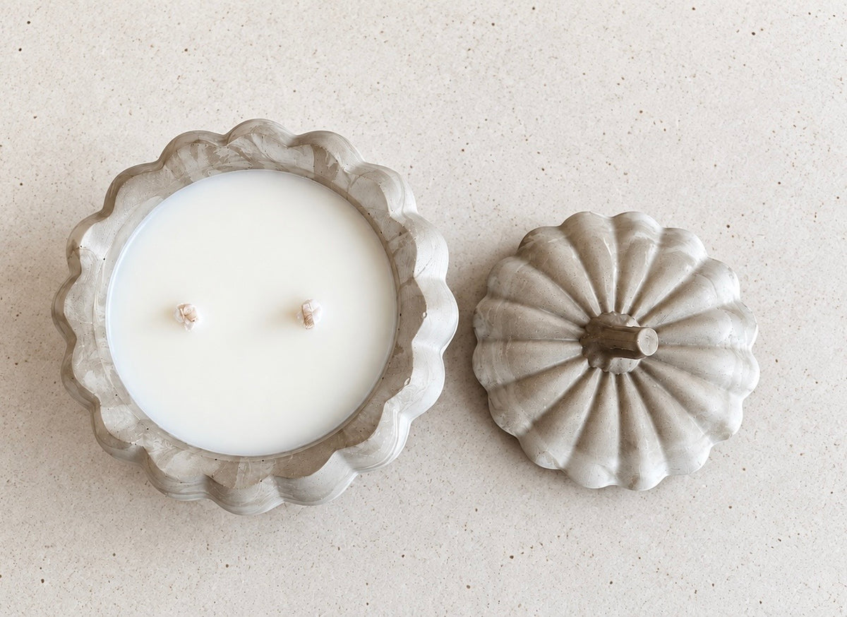 Overhead view of the open pumpkin candle with smooth white wax and two wicks, beside its matching stemmed concrete lid.