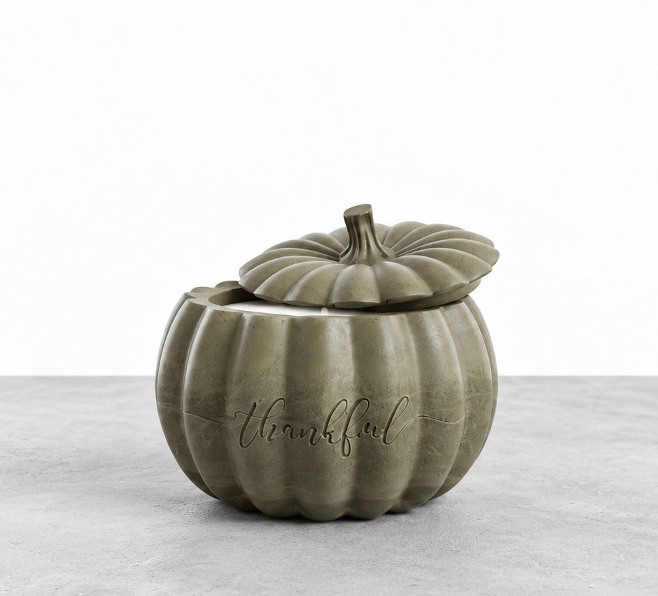 Smoky olive green Thankful pumpkin candle with its matching stemmed lid resting slightly open, revealing the white wax inside.