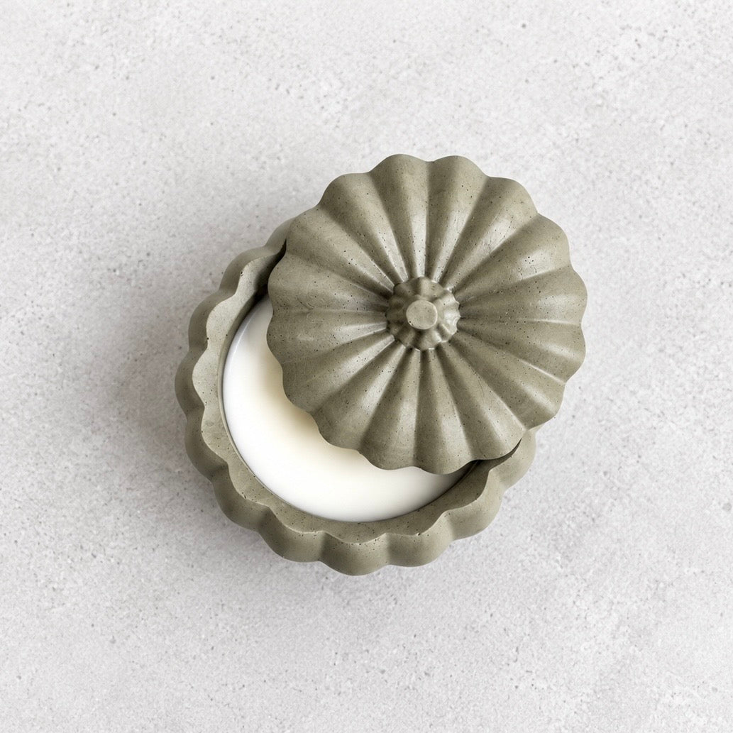 Overhead view of the smoky olive green pumpkin candle, with its ribbed lid partly covering the smooth white wax.