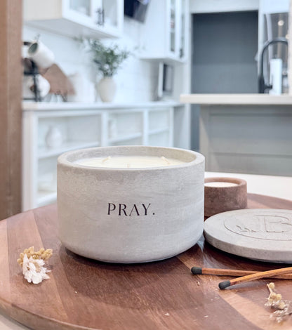 Christian candle with Pray message on wooden table, gray concrete soy candle with lid in home setting