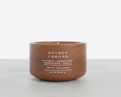 A 12 oz soy wax candle in a matte brown ceramic pot with white text reading 'GOLDEN GROUND' and scent notes for Palo Santo, Sandalwood, Frankincense, and Vanilla, set against a clean white and light gray background.