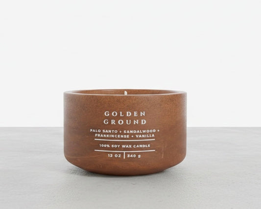 A 12 oz soy wax candle in a matte brown ceramic pot with white text reading 'GOLDEN GROUND' and scent notes for Palo Santo, Sandalwood, Frankincense, and Vanilla, set against a clean white and light gray background.