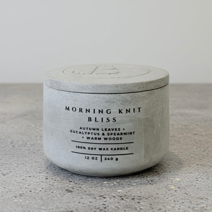 Morning Knit Bliss luxury soy wax candle with engraved concrete lid and handcrafted vessel, scented with autumn leaves, eucalyptus, spearmint, and warm woods.