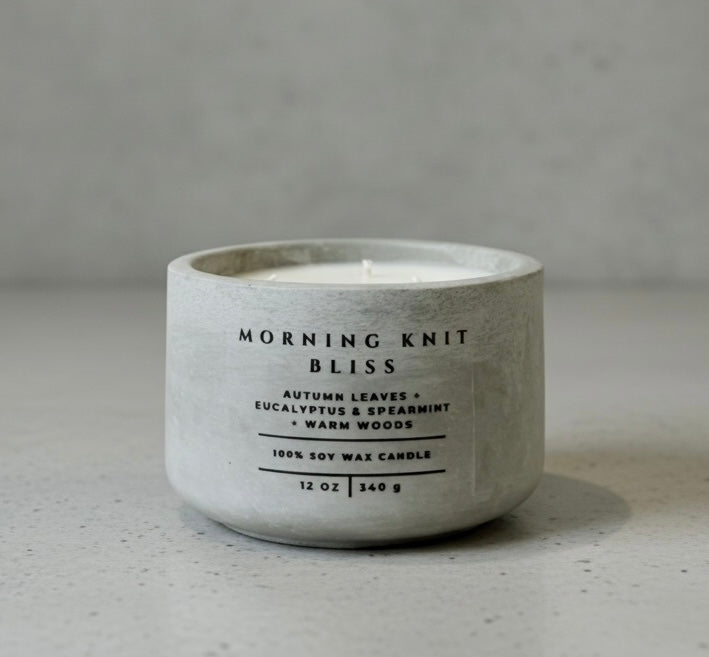 Handcrafted Morning Knit Bliss soy wax candle in a gray concrete vessel, featuring autumn leaves, eucalyptus, spearmint, and warm woods fragrance notes.