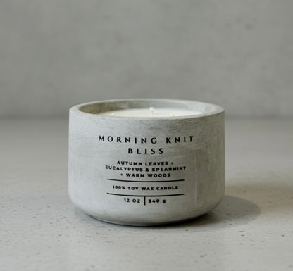 Handcrafted Morning Knit Bliss soy wax candle in a gray concrete vessel, featuring autumn leaves, eucalyptus, spearmint, and warm woods fragrance notes.