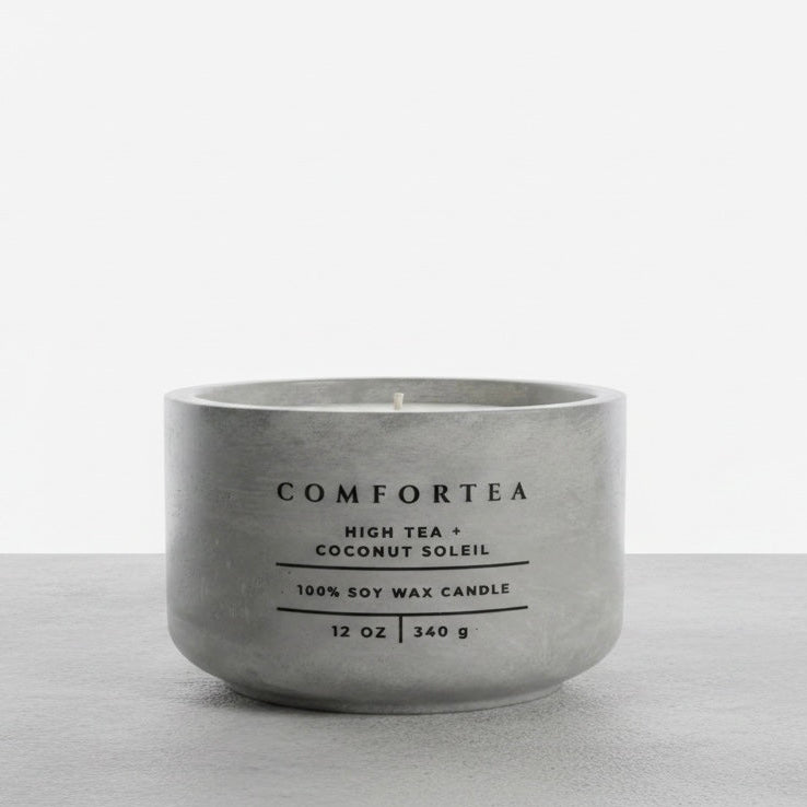 A matte gray concrete-style soy wax candle by COMFORTEA, labeled 'High Tea + Coconut Soleil', on a light gray surface against a white background.