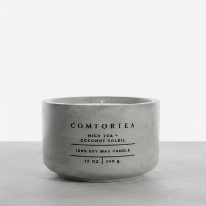 A matte gray concrete-style soy wax candle by COMFORTEA, labeled 'High Tea + Coconut Soleil', on a light gray surface against a white background.