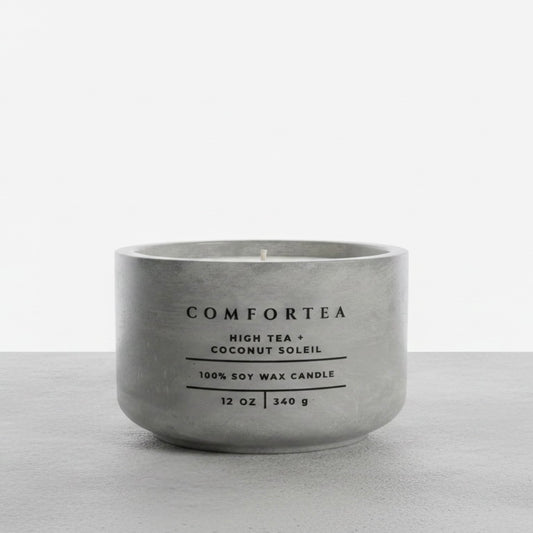 A matte gray concrete-style soy wax candle by COMFORTEA, labeled 'High Tea + Coconut Soleil', on a light gray surface against a white background.