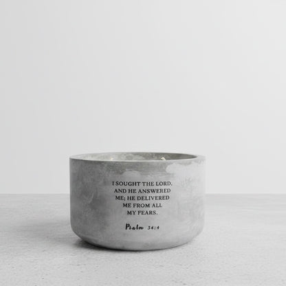 A small round concrete candle with black printed text from Psalm 34:4, set against a clean, light gray background.