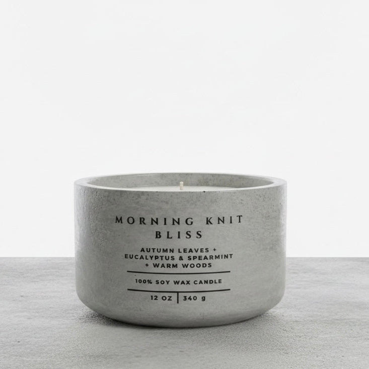 Morning Knit Bliss 12 oz soy wax candle in a handcrafted gray concrete vessel, featuring autumn leaves, eucalyptus, spearmint, and warm woods fragrance notes.