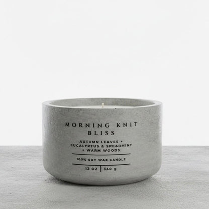 Morning Knit Bliss 12 oz soy wax candle in a handcrafted gray concrete vessel, featuring autumn leaves, eucalyptus, spearmint, and warm woods fragrance notes.