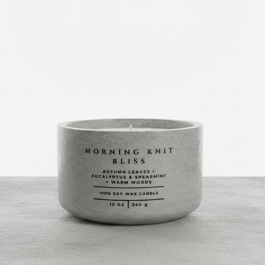 Morning Knit Bliss 12 oz soy wax candle in a handcrafted gray concrete vessel, featuring autumn leaves, eucalyptus, spearmint, and warm woods fragrance notes.